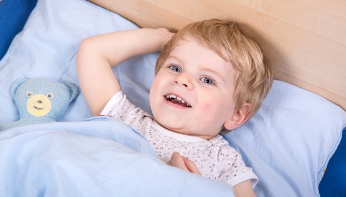 A little boy smiling in his new toddler bed.