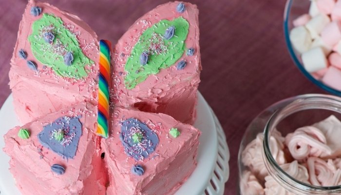 A pink birthday cake made in the shape of a butterfly.