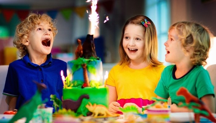 Three children gathered around a dinosaur/volcano birthday cake.