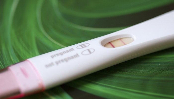 A pregnancy test with a strong positive line and a faint control line on a swirling green background.