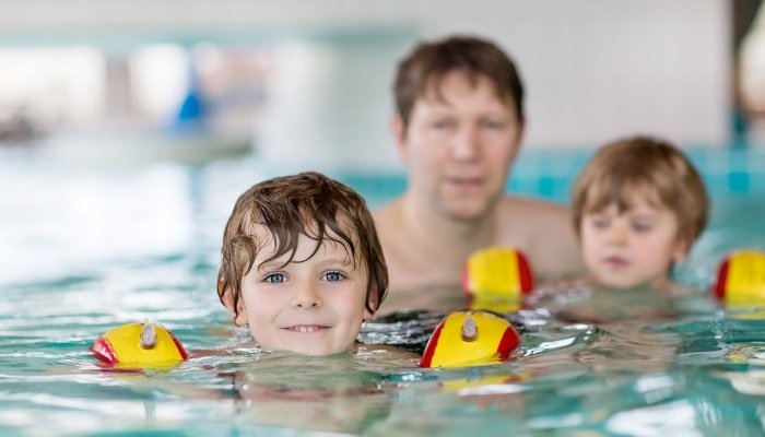 A father in the pool with his sons to keep a watchful eye on them. 