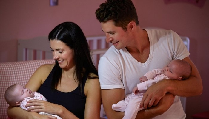 A new mother and father holding their newborn twins in bed.