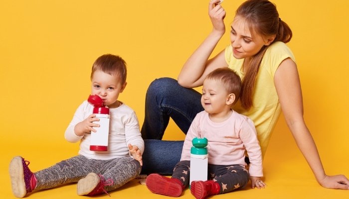 A young mom sitting with her twin girls against a yellow background.