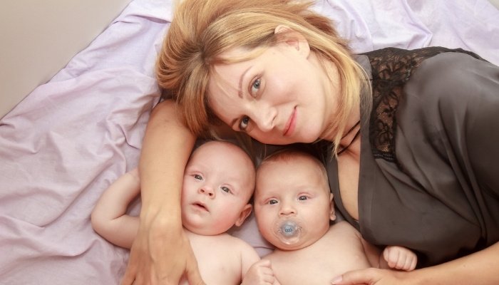 A mother wearing sleepwear while snuggling in bed with her twins.
