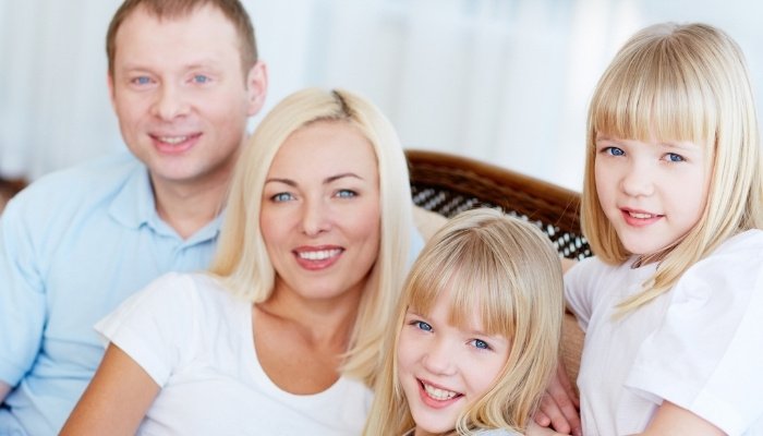 A mother, father and twin girls sitting together on the couch.