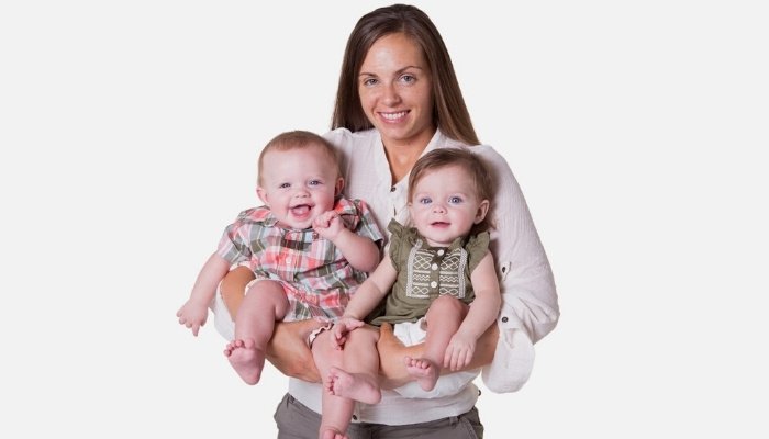 A young mother holding her twins against a white background.