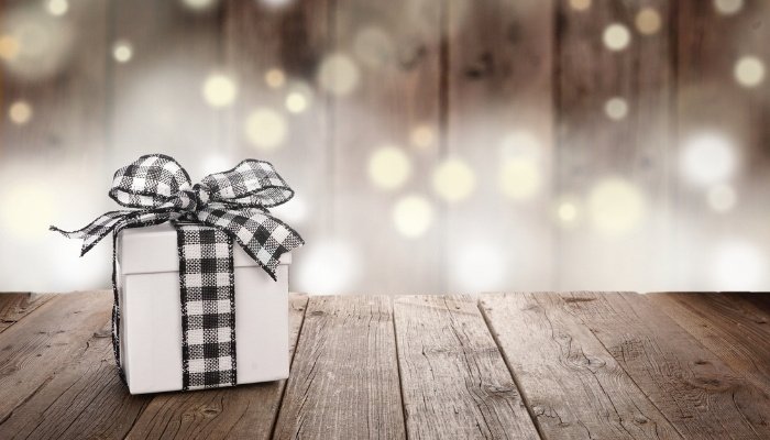 A present with a black and white bow on a table with twinkling lights in the background.