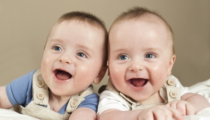 Baby twin boys smiling while lying on their tummies.