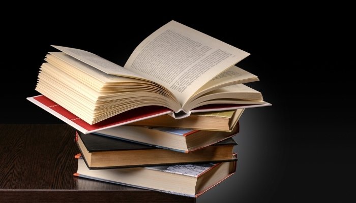 A stack of books on wood table against a black background.