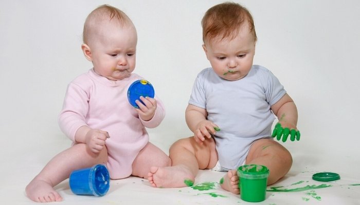 Twin babies finger painting on white background.