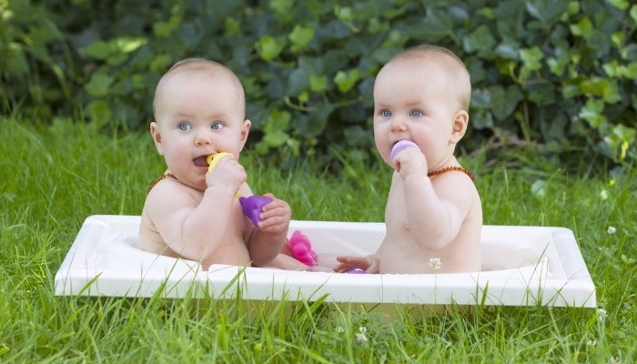 Young twins sitting in an outdoor mini bathtub with toys.