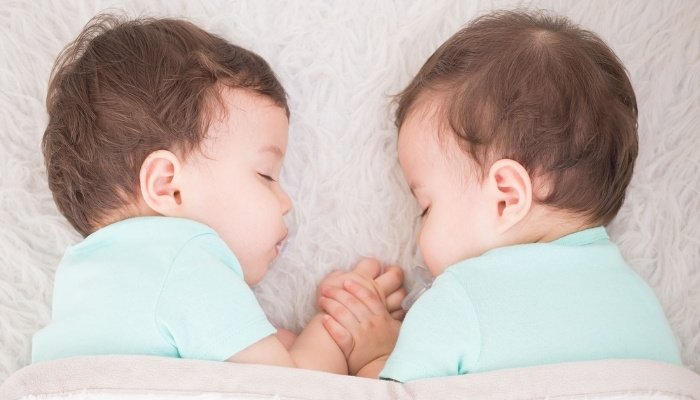 Two twin baby boys napping while holding hands.
