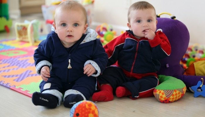 Year-old twin brothers in jackets sitting in a nursery with toys.