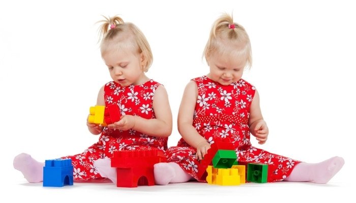Two little twin sisters in red flowery outfits playing with plastic blocks.