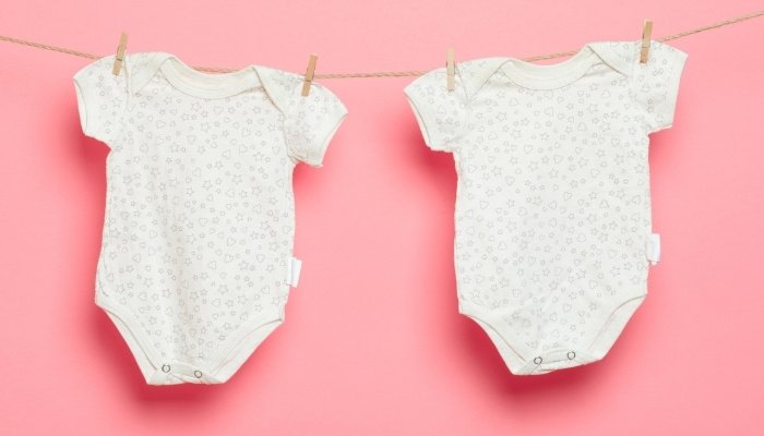 Two newborn onesies hanging from a clothesline against a pink background.