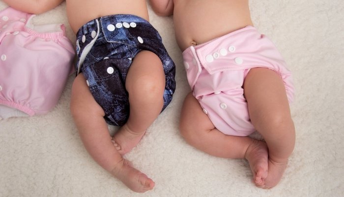 Baby twins wearing blue and pink cloth diapers.