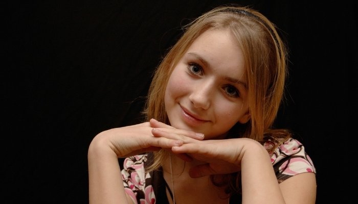 A smiling 12-year-old girl against a black background.