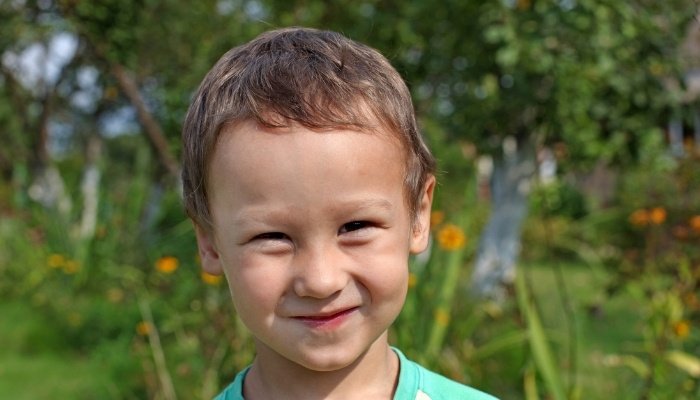 A smiling 4-year-old boy standing outside.