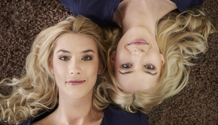 Adult twin sisters with blonde hair lying head to head facing opposite directions.