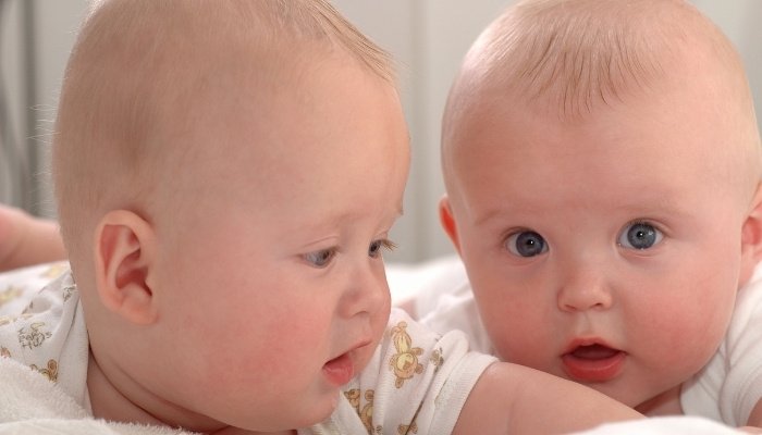 A close look at a set of adorable twin babies having tummy time on a bed.