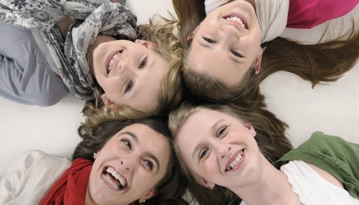 Four young teenage girls lying down with their heads touching to form an X shape.