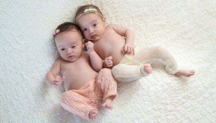 Infant fraternal twin sisters lying on a white blanket wearing only pants.