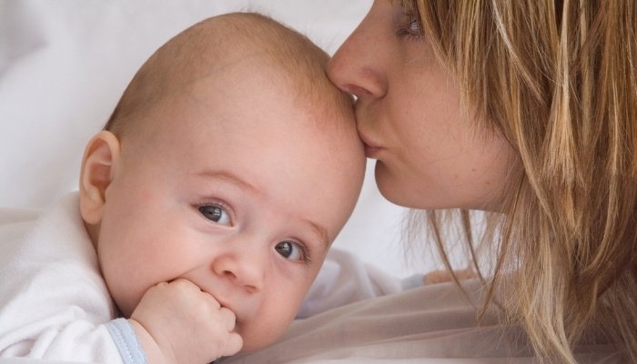 Close-up of a mother giving her baby a kiss on the head.