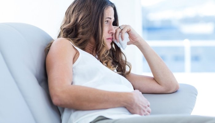 A pregnant woman sitting on a couch crying softly.