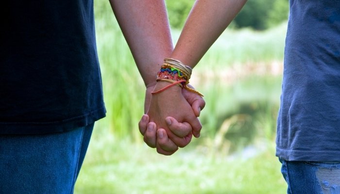 Close up of a teen boy and teen girl holding hands.