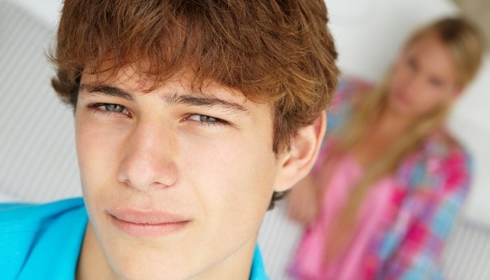 A teenage boy with a girl blurred in the background.