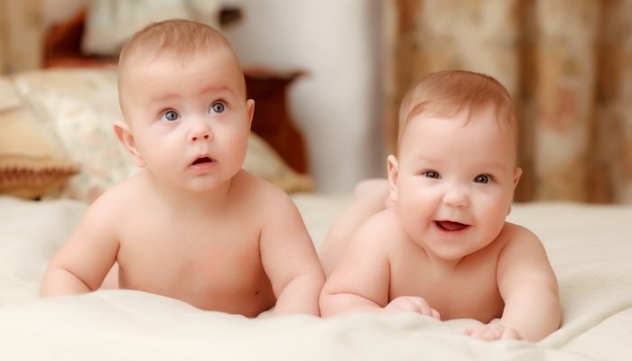 Two cute twin babies lying on their stomachs on their parent's bed.