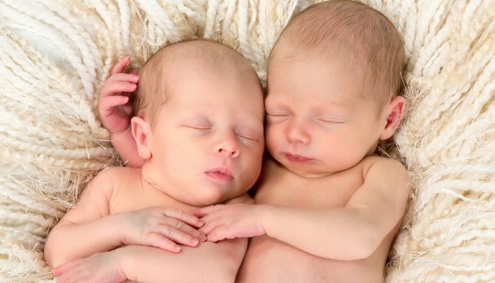 Newborn twin babies snuggling together on a cozy blanket.