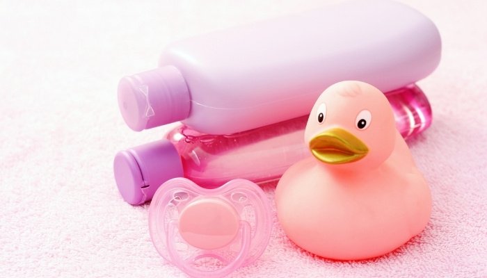 A pink rubber ducky and pacifier lying in front of baby wash and shampoo bottles.