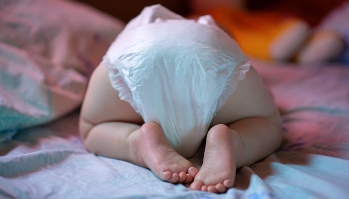 An older baby sleeping on his knees with his diapered rear end up in the air.