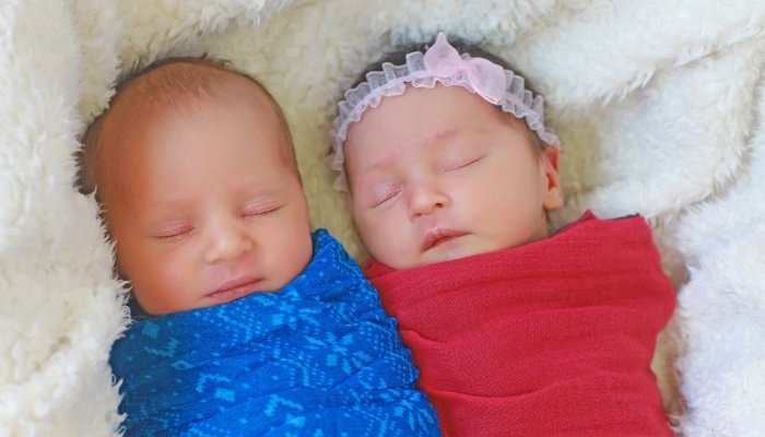 Infant fraternal twins wrapped in red and blue blankets.