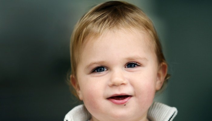 A cute toddler with a slight smile on her face against a gray background.