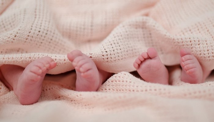 The feet of premature twins sticking out from under a pink blanket.