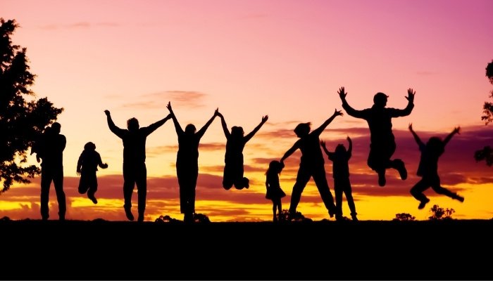 Two parents and eight children jumping for a photo with a gorgeous sunset in background.