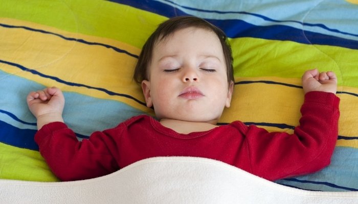 A toddler boy in red pajamas sleeping sprawled out in bed.