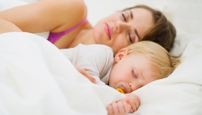A young mother sleeping beside her little boy under a white blanket.