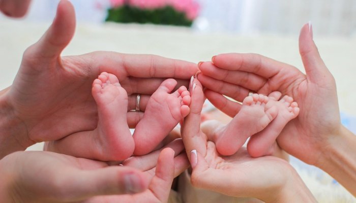 A new mother and father cradling their newborn twins' feet in their hands.