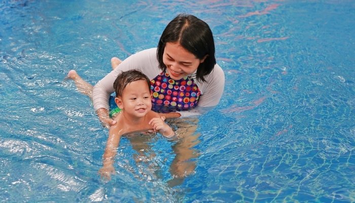 A mother holding her toddler in the water during a swim class.