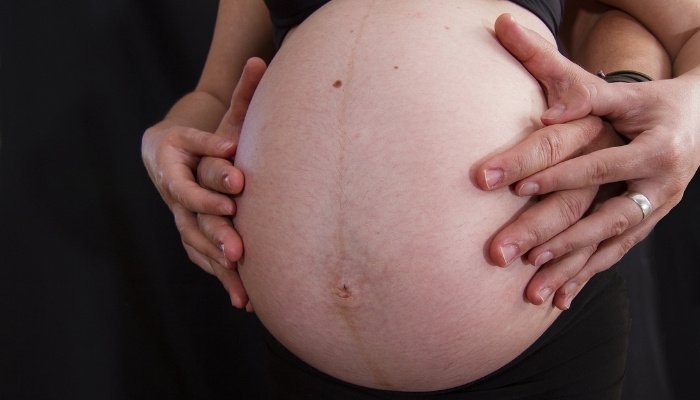 A mother and father placing their hands on the mother's very large pregnant belly.