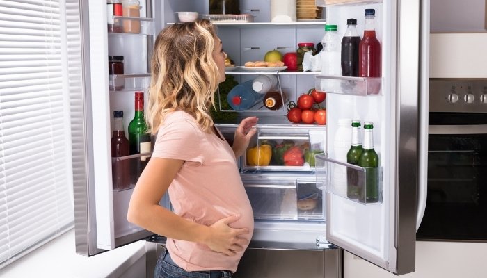 A pregnant lady scanning the fridge for a snack.