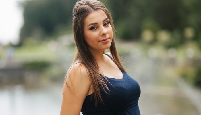 A slightly smiling pregnant lady in a casual black dress standing outside.