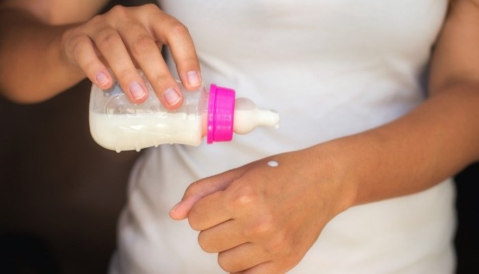 A woman testing baby bottle temperature by dropping some milk on her wrist.