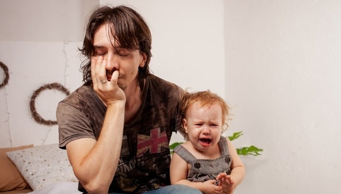 A tired, frustrated dad holding a hysterical baby by his side.