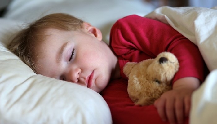 A cute toddler asleep in bed holding a teddy bear tightly.
