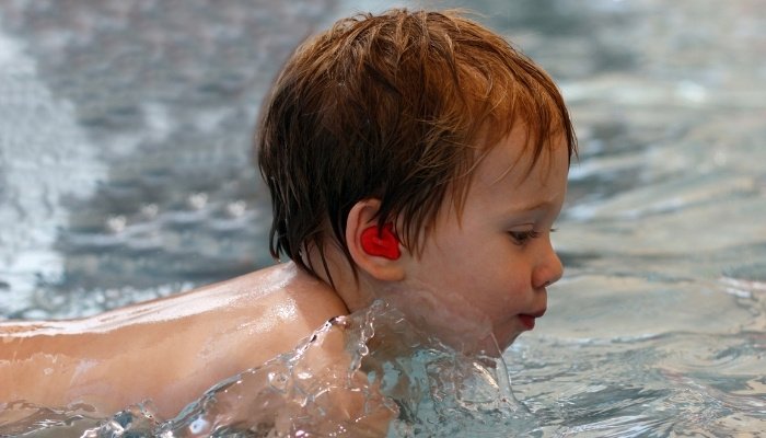 A little boy with red hair playing in a swimming pool.