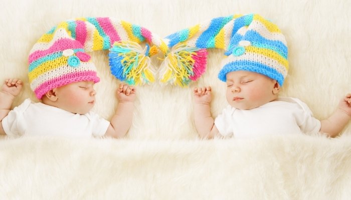 Twin brother and sister babies wearing pink and blue stocking caps.